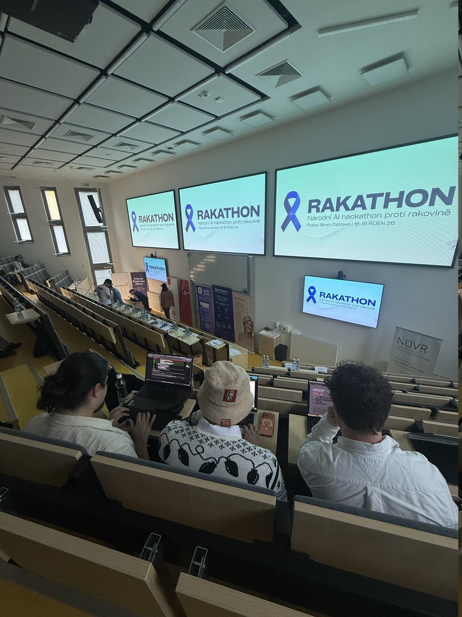 Team Canbe working on laptops in a lecture hall at Rakathon 2026, with Rakathon screens in the background